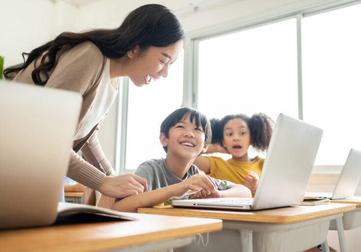 Young Asian Female teacher helping pupils using laptop during computer class in international elementary school. Browsing Internet, Modern classroom, Education, Online Learning, E-Learning Concept